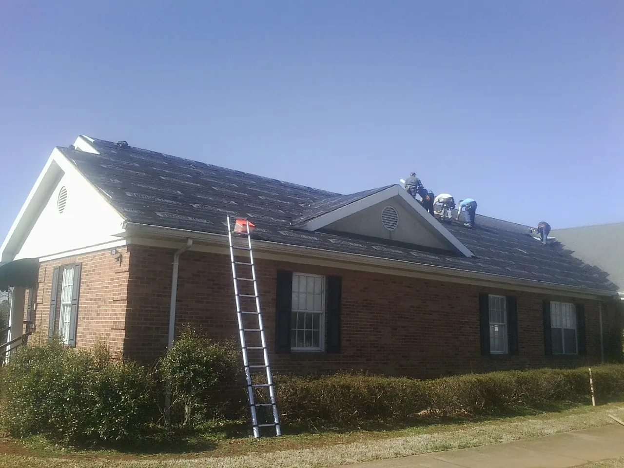Crew tearing shingles off a brick ranch roof with a ladder set — Emergency Roof Repair work by our crew in Martin