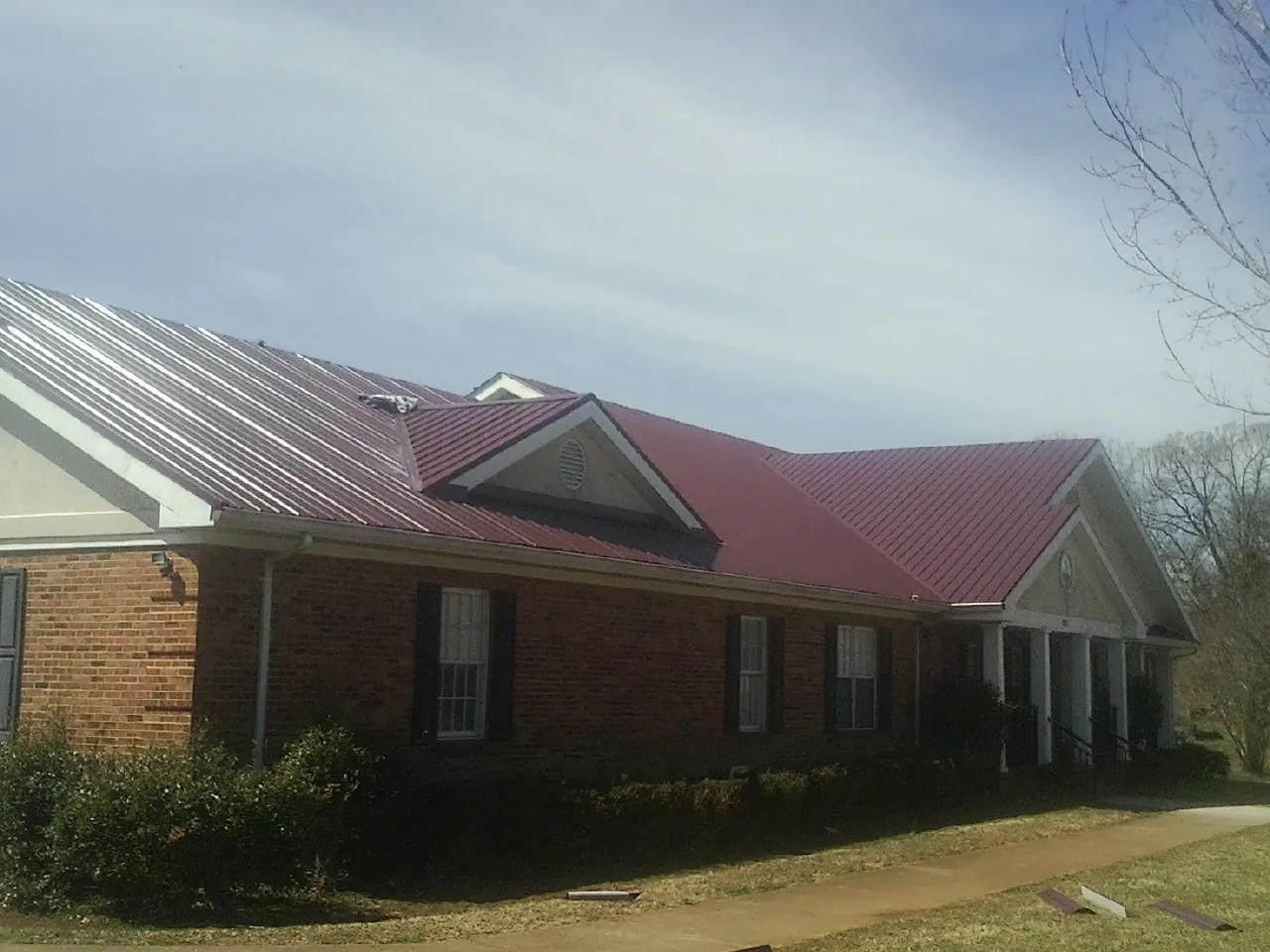 Red metal roof with gabled entries on a long brick building, from a Hail Damage Roof Repair job in Martin
