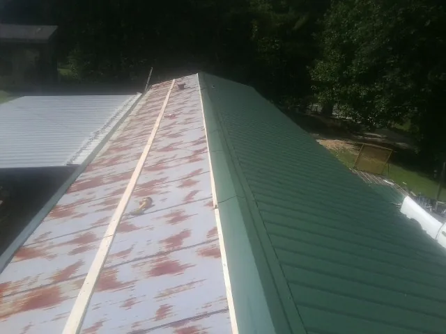 Old rusted panels beside newly installed green metal roofing — Wind Damage Roof Repair by Roofing Brothers in Martin